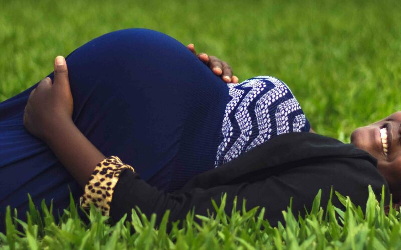 Pregnant woman laying on grass smiling holding her bump