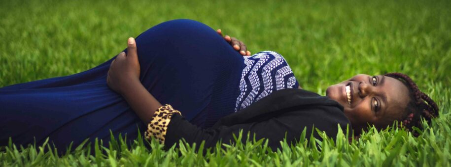 Pregnant woman laying on grass smiling holding her bump